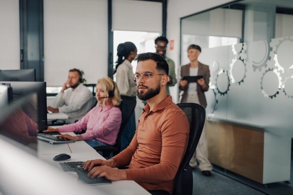 Busy contact center floor with agents on calls and a supervisor holding a tablet, illustrating contact center staffing cost