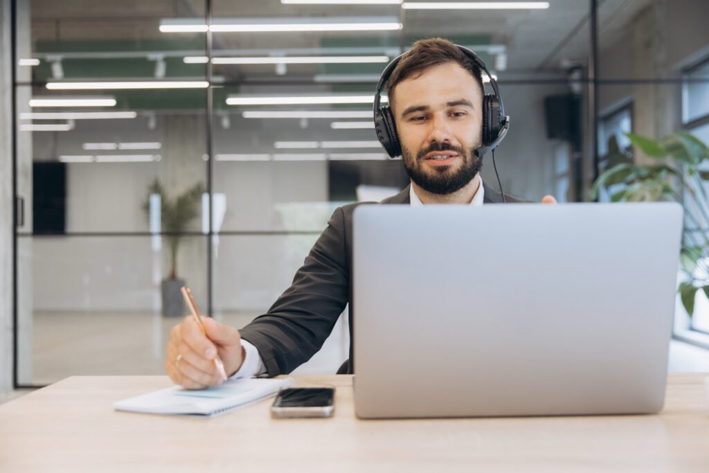 Contact center agent with a headset taking notes at a laptop in an office run with a modern WFM platform